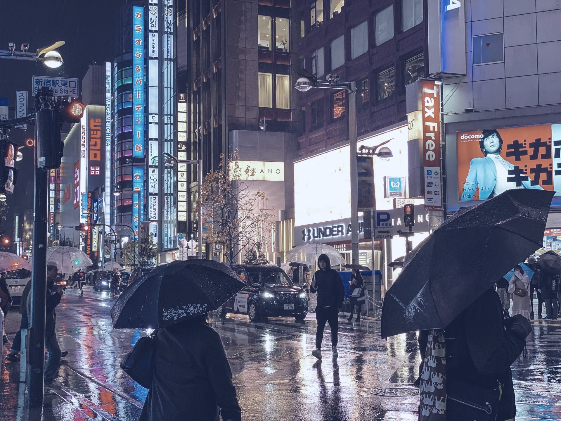 Yağmurlu bir gecede Tokyo sokağında şemsiyeli yayalar ve tabelalar