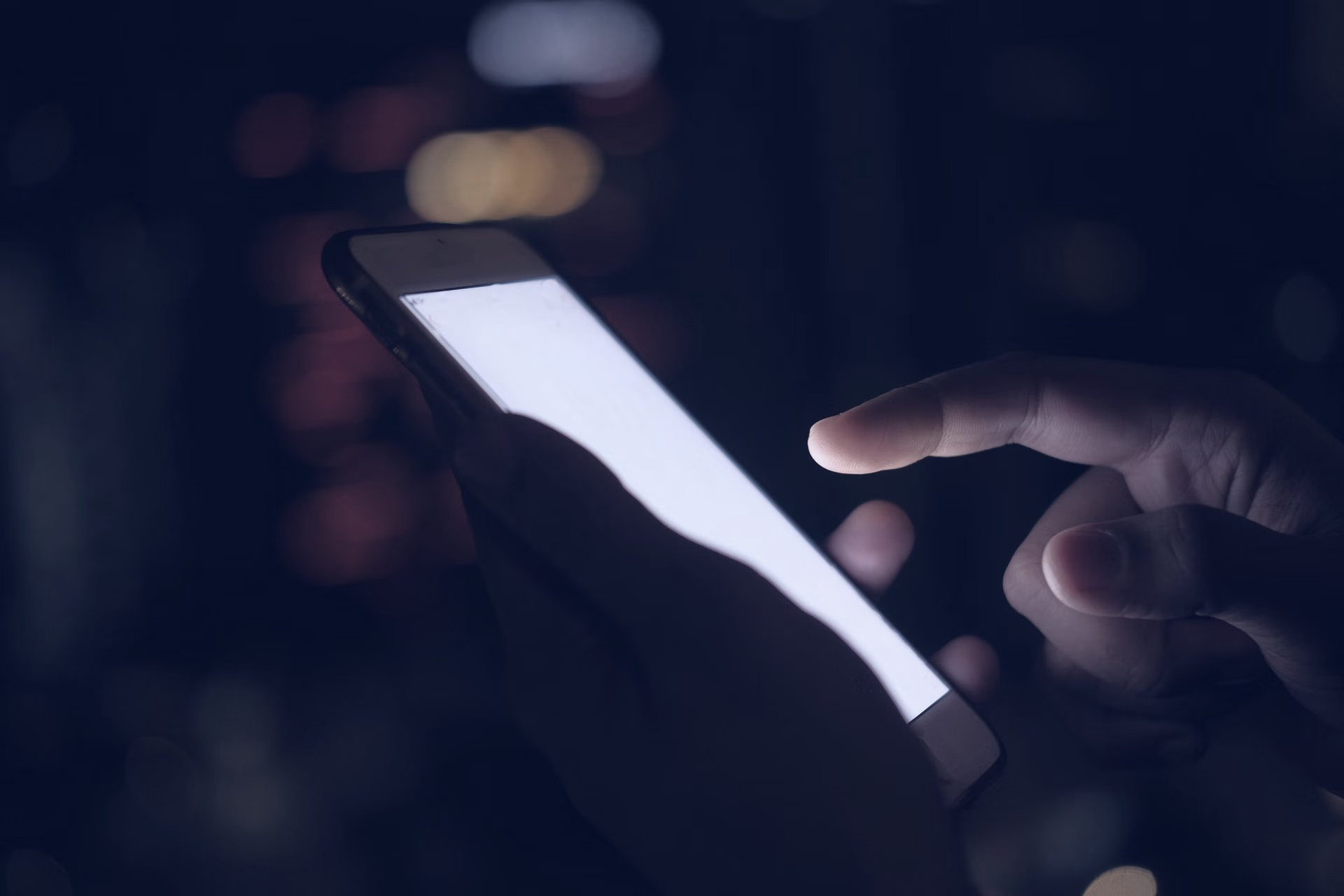 Gece şehir ışıkları önünde akıllı telefon kullanan el